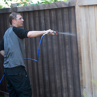Muž provozující aktivitu natírání plotu stříkacím zařízením