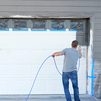 Man spray painting a garage door with an airless sprayer