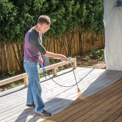 Man applying stain to decking using a sprayer with tip extension